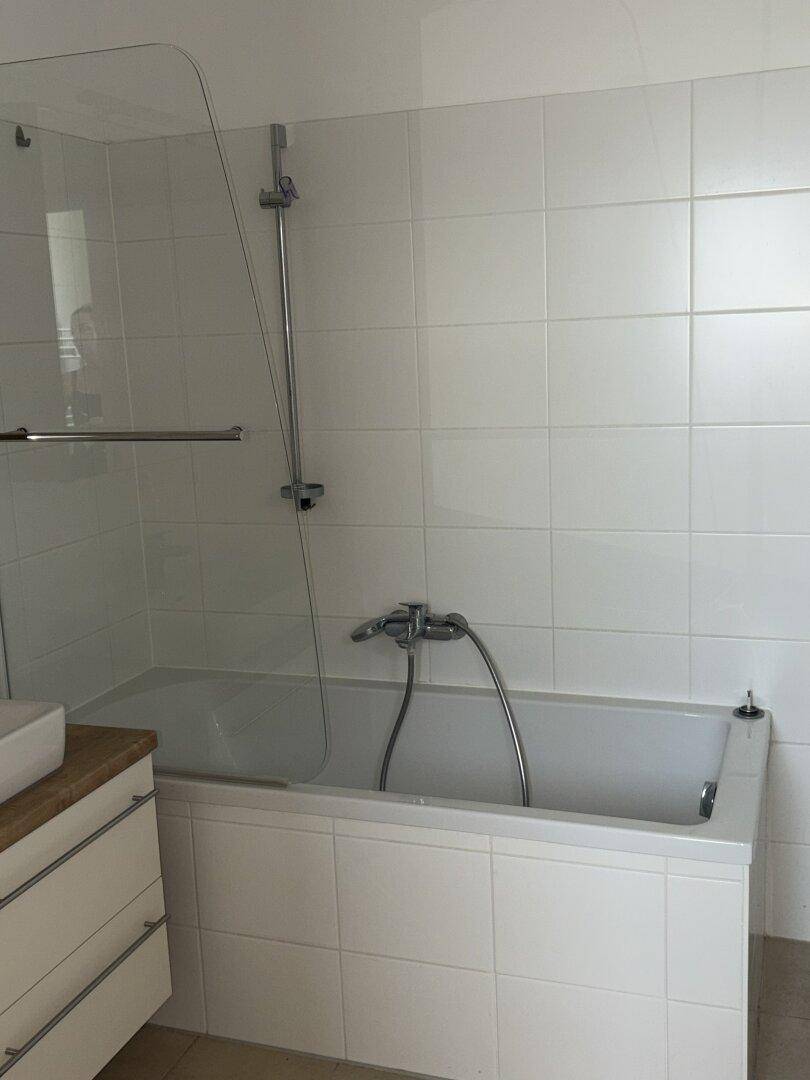 Badewanne mit Duschfunktion und Glasabtrennung in einem gefliesten Badezimmer.