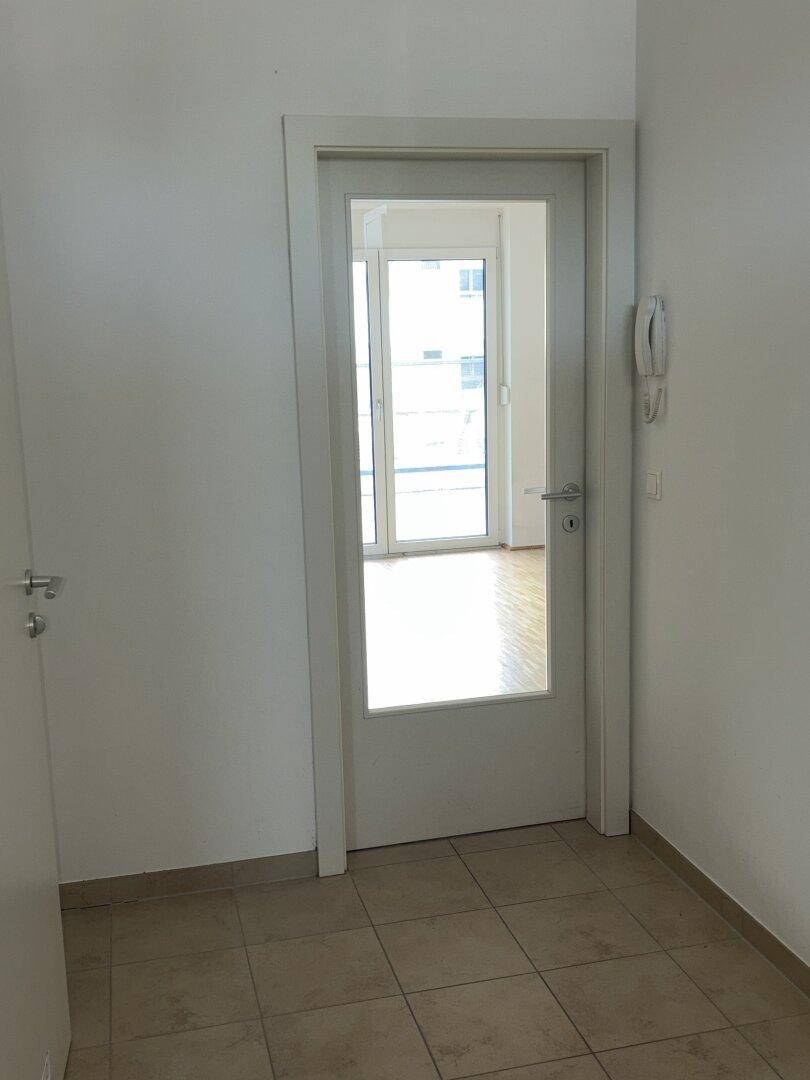 Heller Flur mit Fliesenboden und einer Tür mit Glaseinsatz, die zu einem weiteren Raum führt.