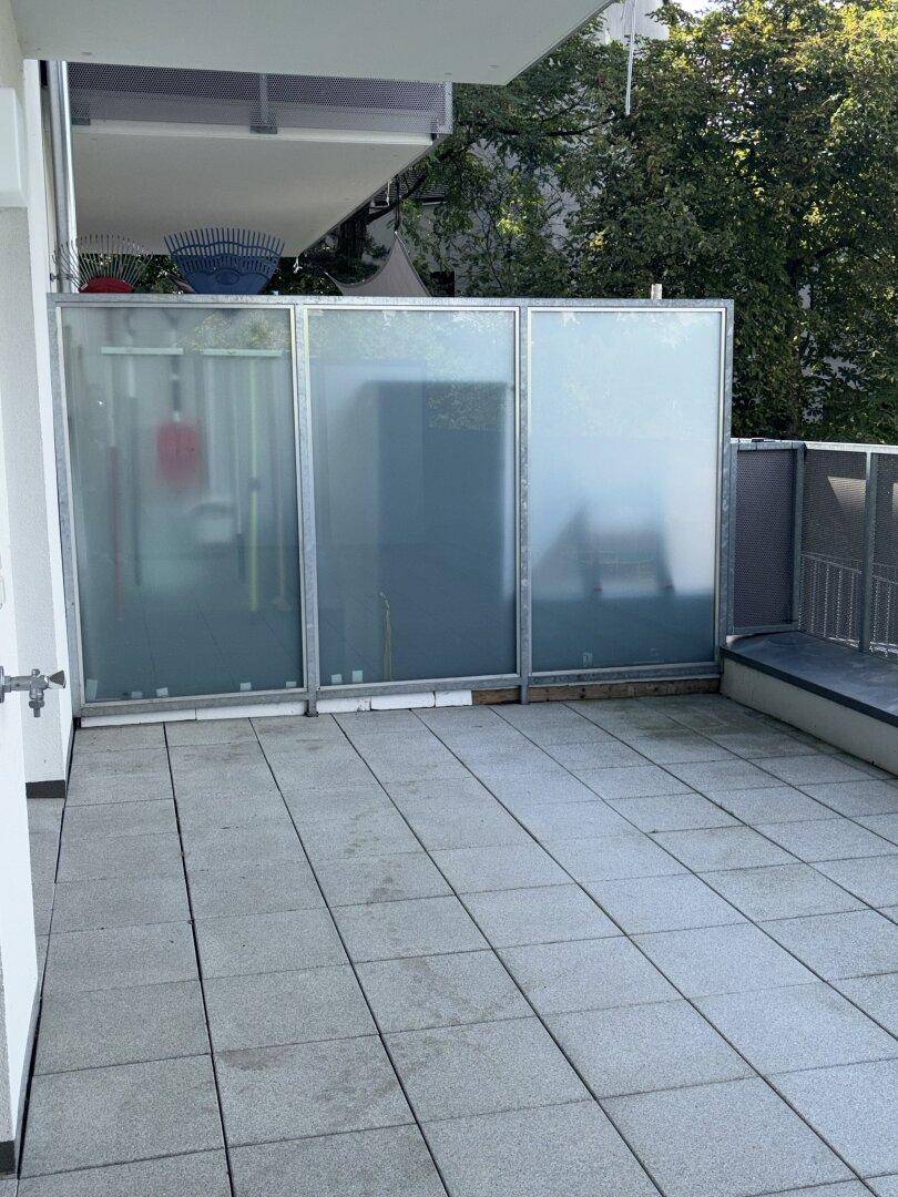 Geräumige Terrasse mit Fliesenboden und Milchglas-Sichtschutzelementen.