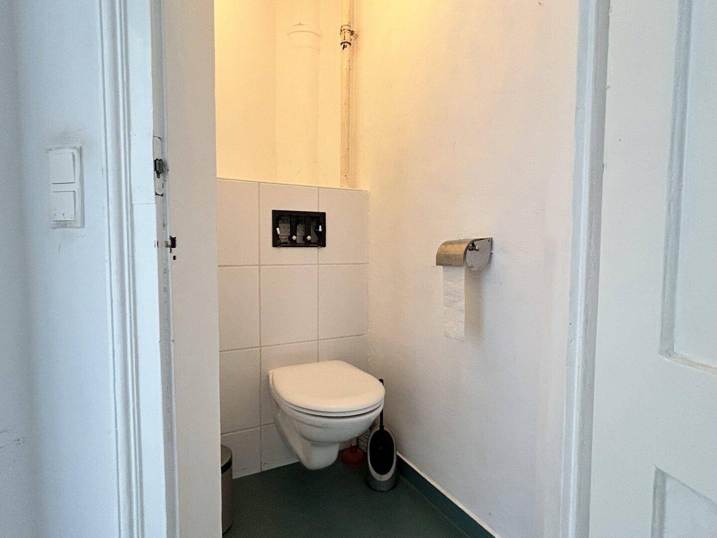 Separate Toilette mit Wand-WC und weißen Fliesen, funktional und sauber.