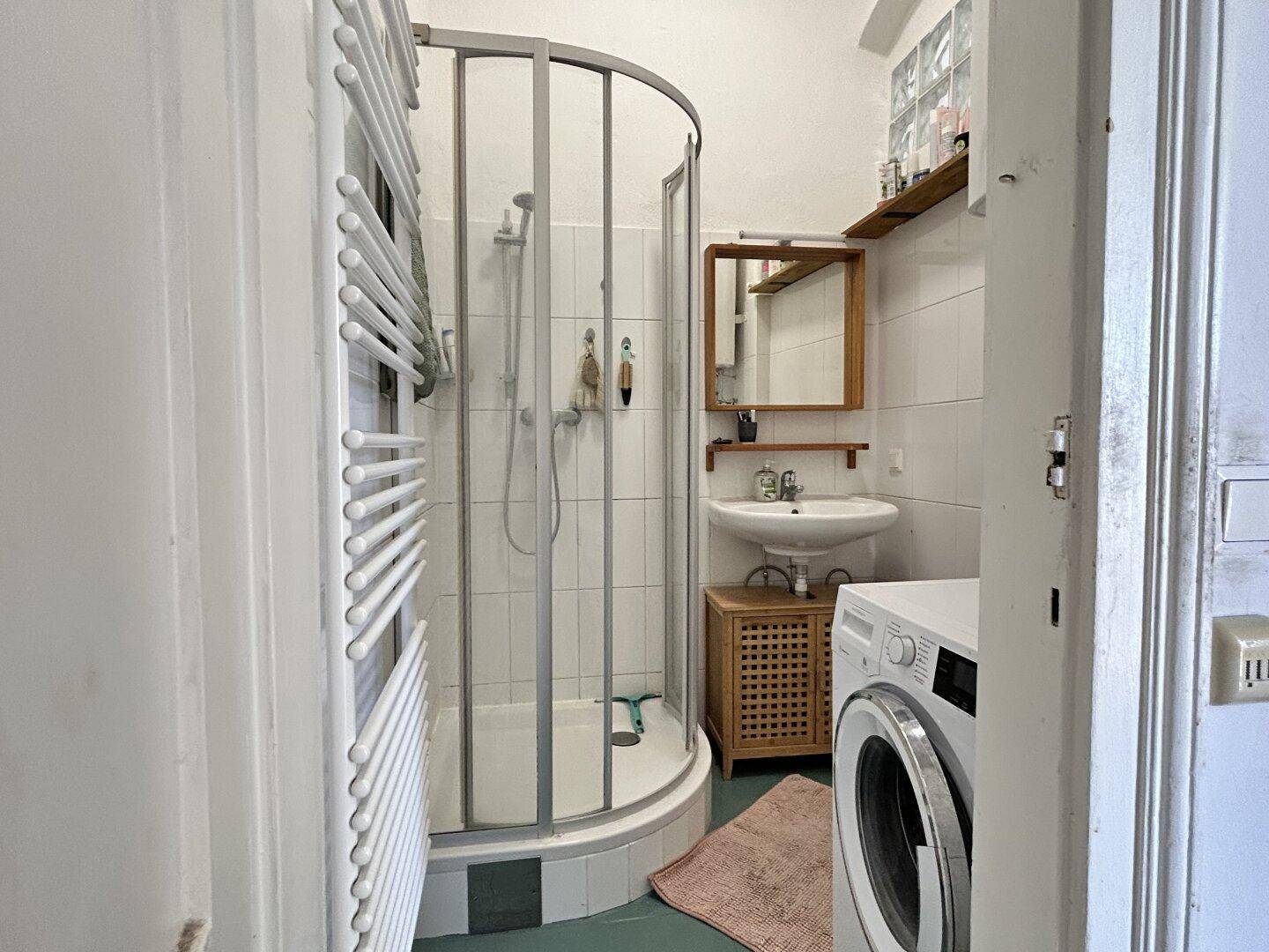 Badezimmer mit Duschkabine, Waschbecken, Waschmaschine und Handtuchheizkörper.