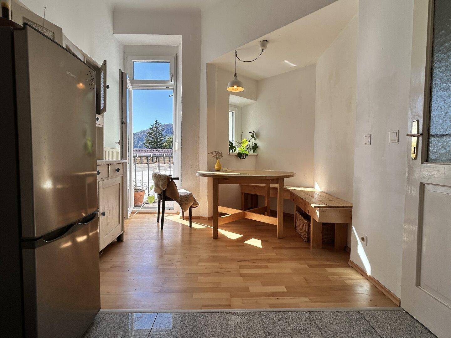 Helle Wohnküche mit Esstisch, Holzboden und Zugang zu einem Balkon mit Bergblick.
