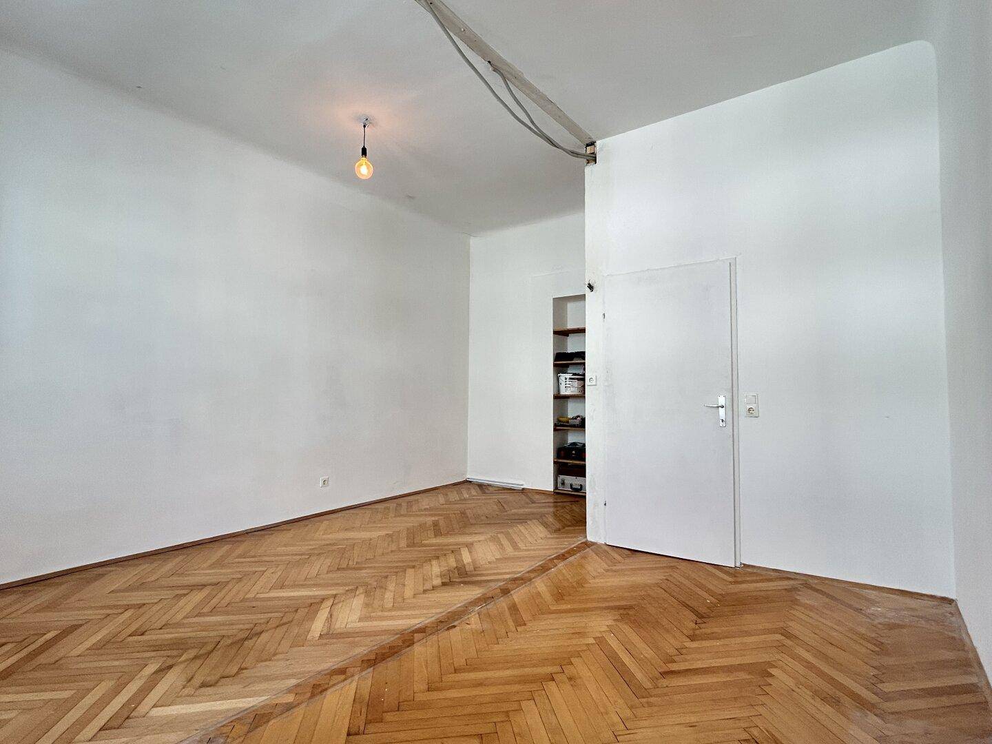 Heller Raum mit Fischgrätparkett, weißen Wänden und einer praktischen Nische mit Regal.
