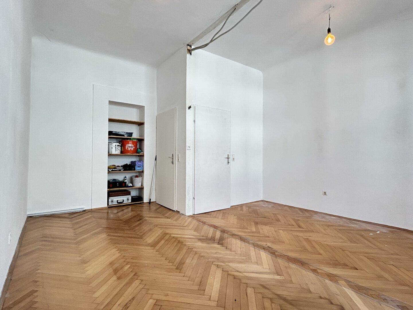 Heller Raum mit Fischgrätparkett, weißen Wänden und einer Nische mit Regal.