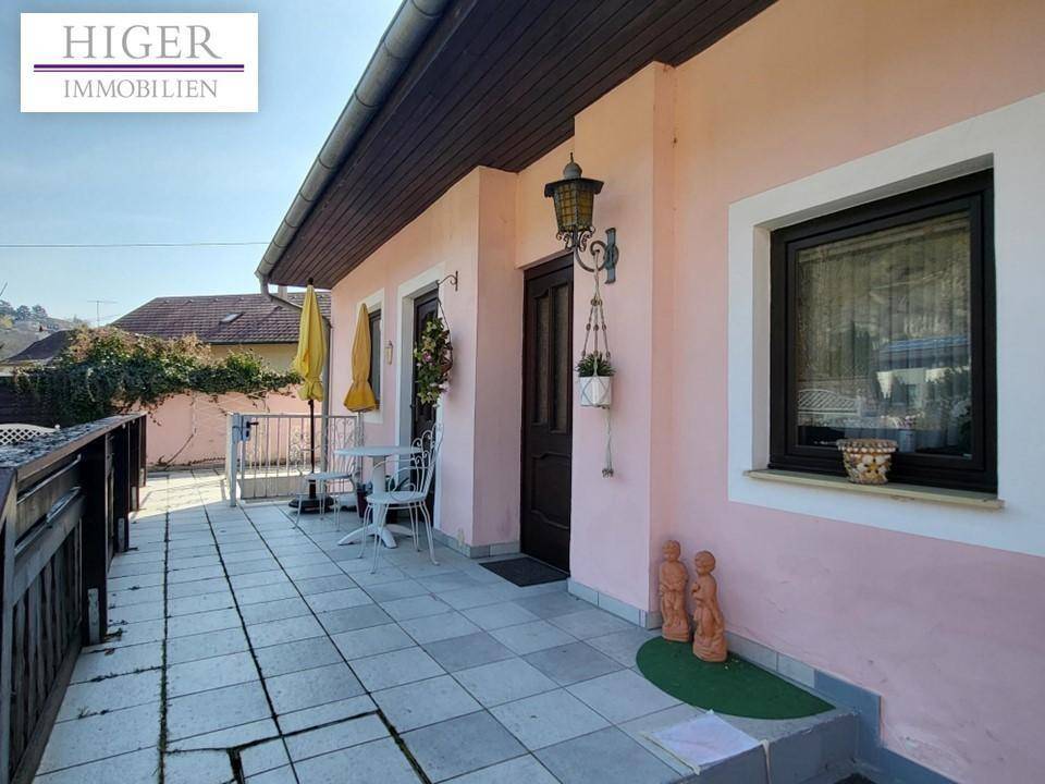 Geflieste Terrasse mit Sitzgelegenheiten und Sonnenschirm, ideal für entspannte Stunden im Freien.
