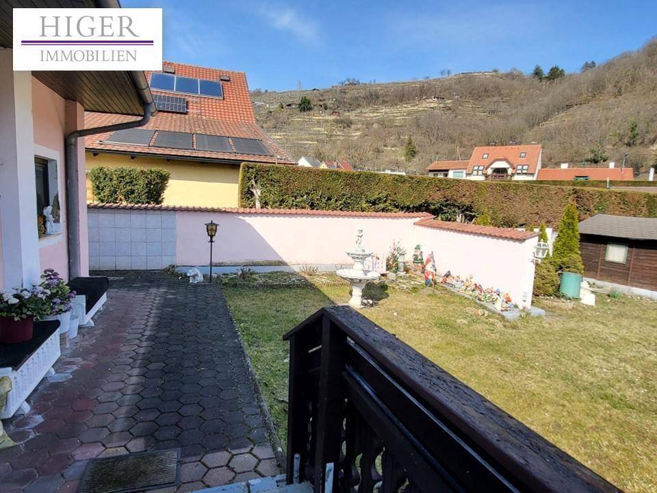 Gepflegter Gartenbereich mit Rasenfläche, Zierbrunnen und Hecke, umgeben von einer Mauer.