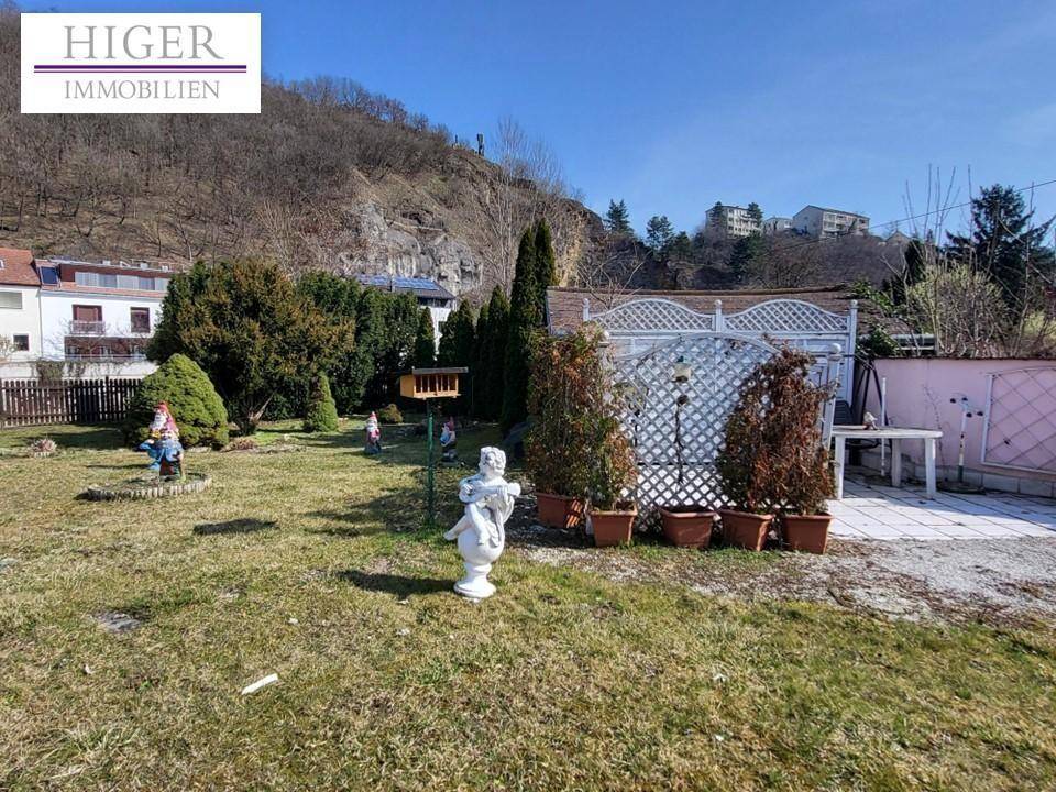 Weiterer Teil des Gartens mit Zierfiguren, Topfpflanzen und Blick auf die bewaldeten Hügel.