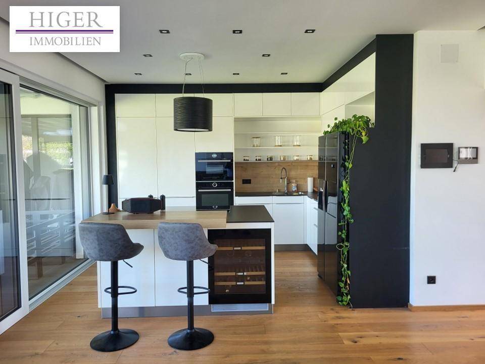 Moderne Küche mit weiß-schwarzen Fronten, Kücheninsel und Holzboden, offen zum Wohnbereich.