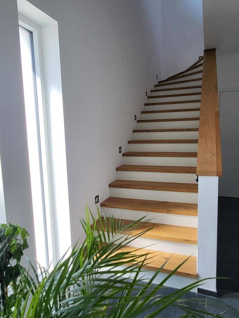 Moderne Holztreppe mit indirekter Beleuchtung und großem Fenster, das den Bereich erhellt.