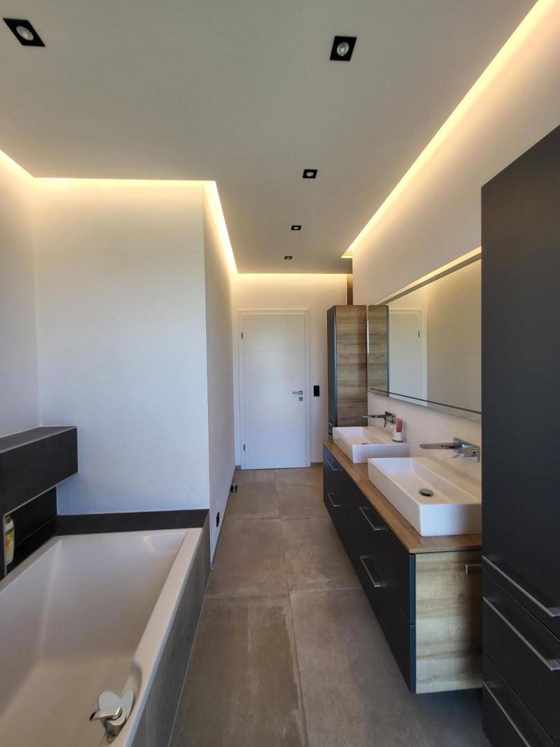 Modernes Badezimmer mit Doppelwaschbecken, Badewanne und indirekter Beleuchtung.