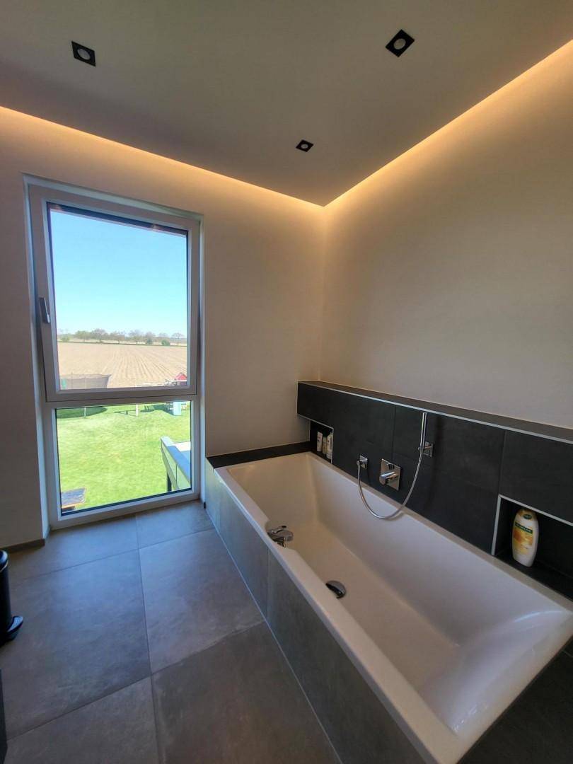 Helles Badezimmer mit eingebauter Badewanne und großem Fenster mit Blick ins Grüne.
