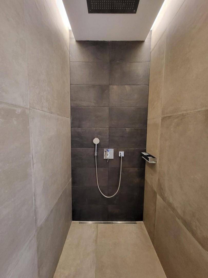 Geräumige begehbare Dusche mit Regenduschkopf und modernen Fliesen in Grautönen.