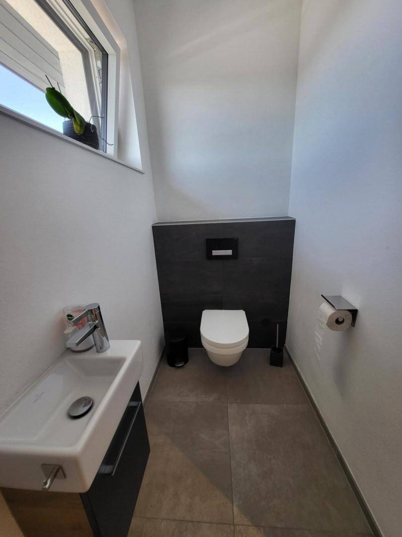 Kleines Gäste-WC mit wandhängender Toilette, kleinem Waschbecken und Fenster.