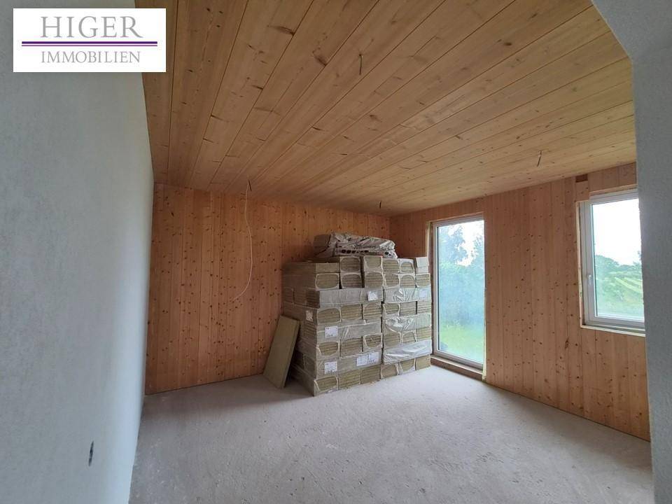 Zimmer mit Holzwänden und Holzdecke, großen Fenstern und Baumaterialien, noch im Rohbau.