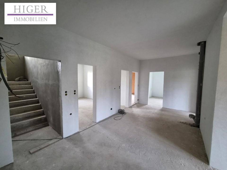 Großer unfertiger Raum mit Betonboden und Zugang zu weiteren Zimmern, bereit für den Innenausbau.
