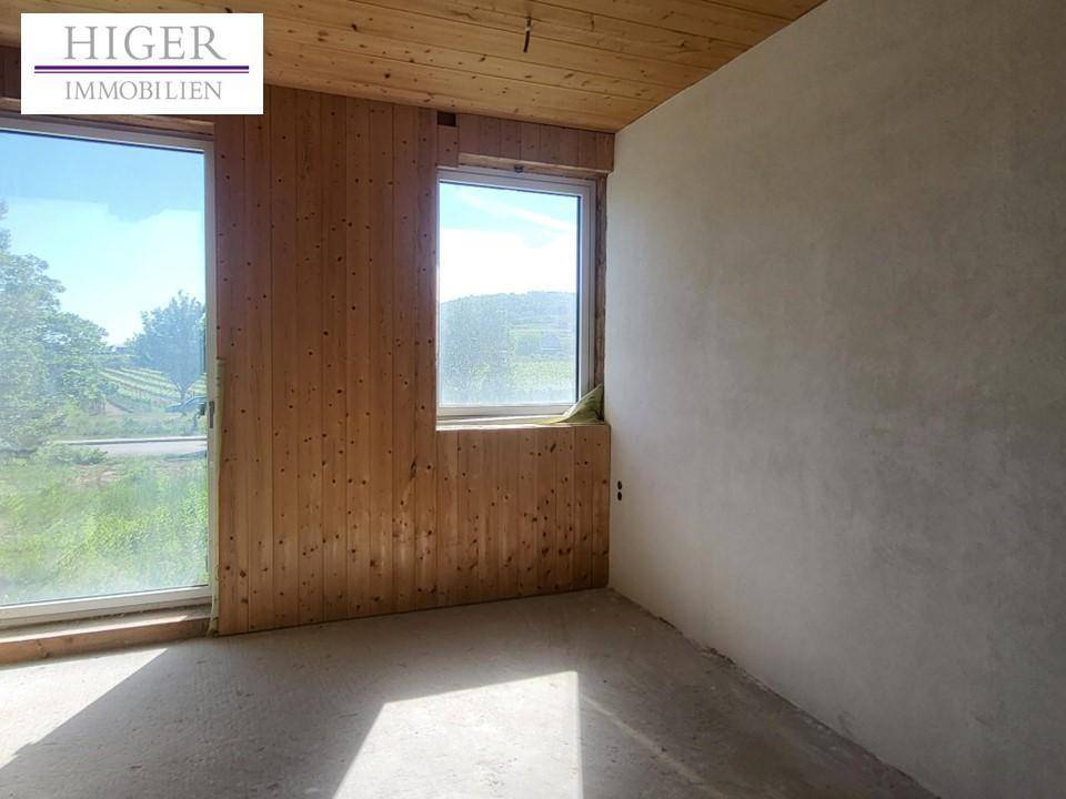 Zimmer mit Holzwänden, großen Fenstern und Blick auf die Landschaft, noch im Rohbau.
