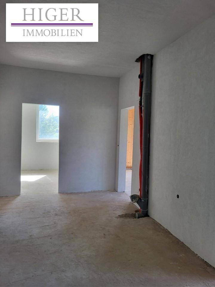 Unfertiger Innenraum mit Betonboden und sichtbaren Rohren an der Wand, bereit für den Ausbau.
