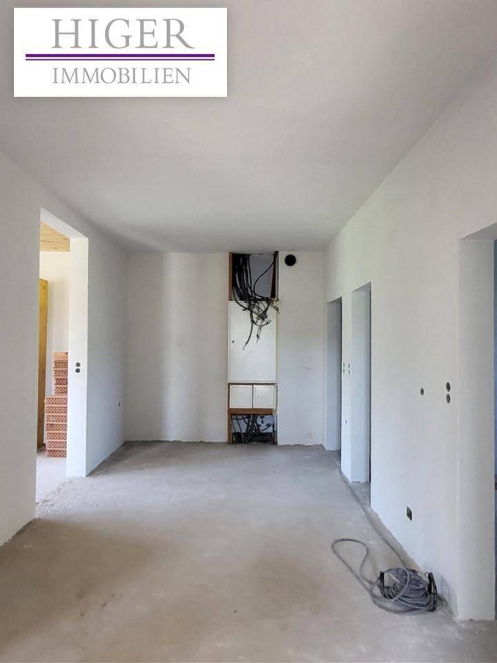 Unfertiger Innenraum mit weißen Wänden, Betonboden und sichtbaren Kabeln, bereit für den Ausbau.