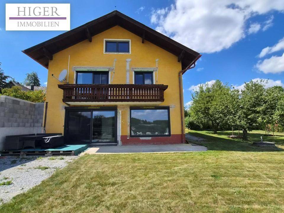 Gelbes Wohnhaus mit Balkon, großen Fenstern und weitläufigem Gartenbereich.