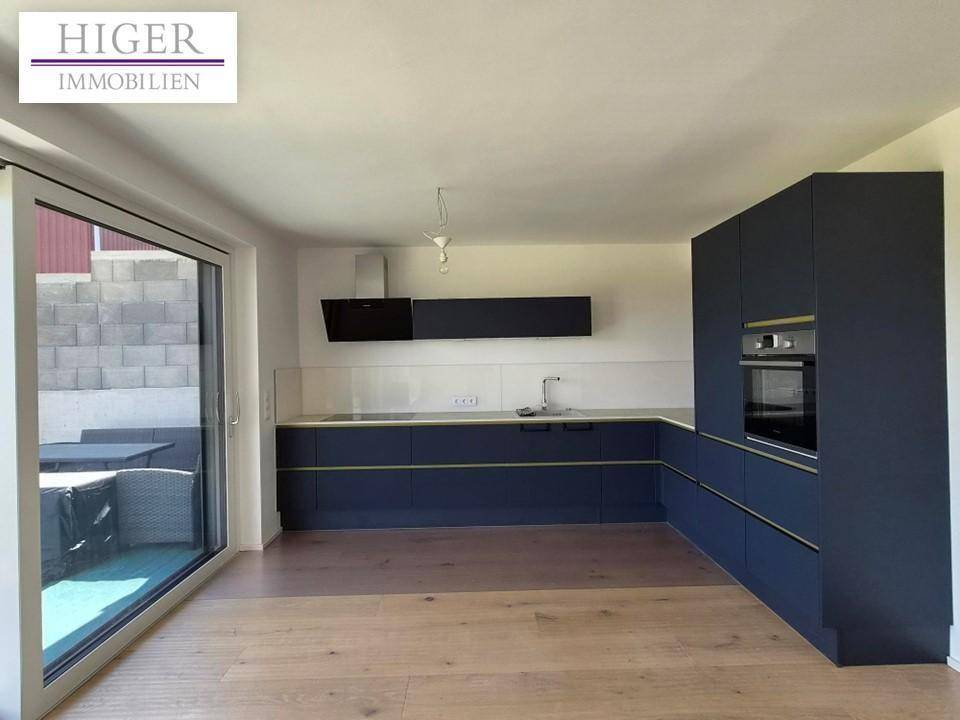 Moderne Küche mit dunkelblauen Schränken, integrierten Geräten und Zugang zur Terrasse.
