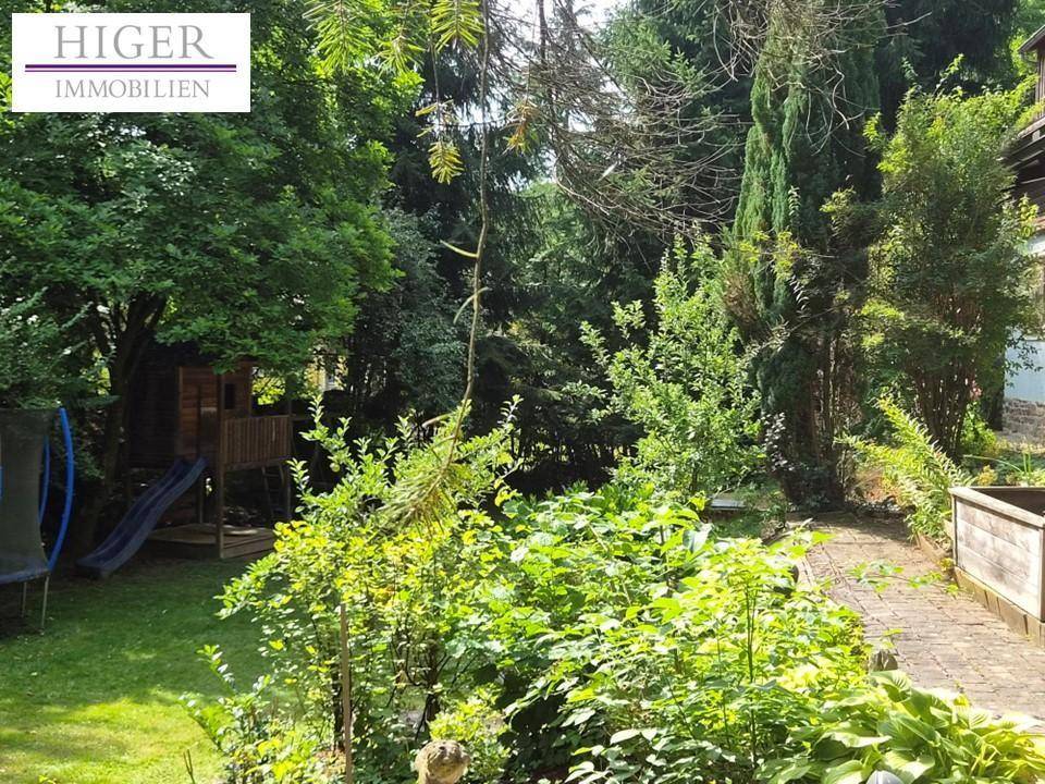 Grüner Garten mit Trampolin, Spielhaus und üppiger Vegetation, ideal für Familien.