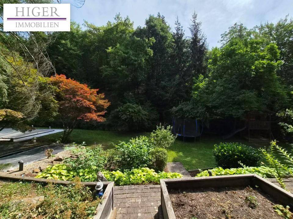 Großer Garten mit Rasen, Bäumen und Spielgeräten, umgeben von viel Natur.