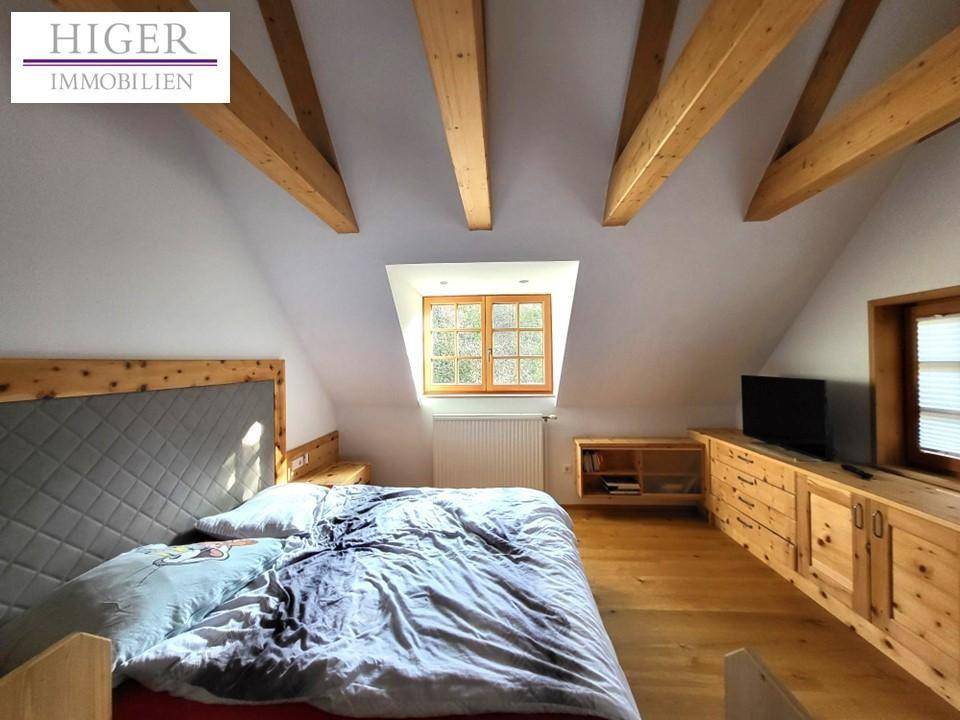 Schlafzimmer im Dachgeschoss mit Holzbalken, Holzboden und Dachfenster.