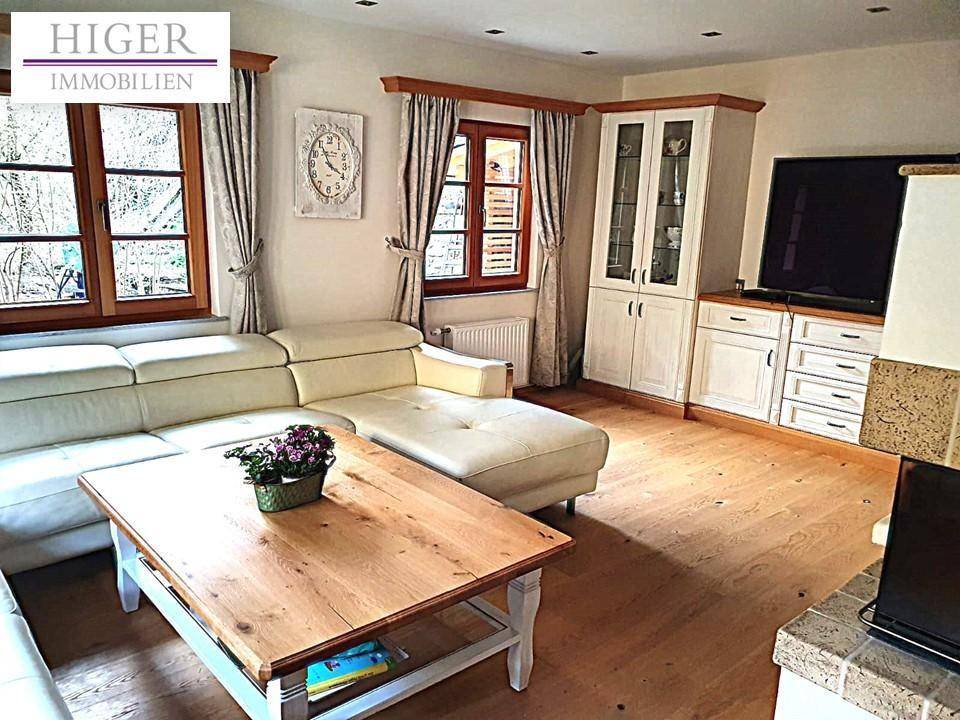 Gemütliches Wohnzimmer mit großem Sofa, Holzboden und Blick in den Garten.