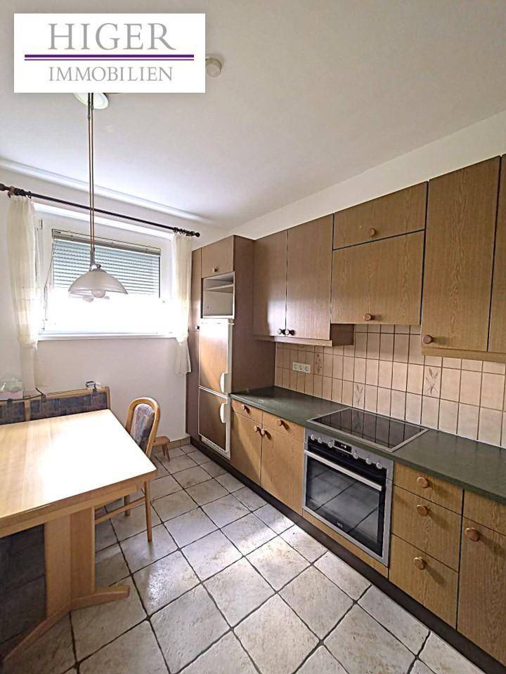 Funktionale Küche mit Holzschränken, Fliesenboden und einem kleinen Essbereich am Fenster.