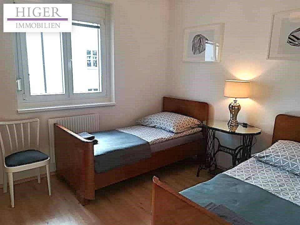 Helles Schlafzimmer mit zwei Einzelbetten, Parkettboden und großem Fenster.