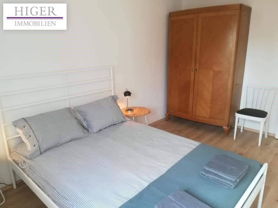 Schlafzimmer mit weißem Bettgestell, Holzkleiderschrank und Parkettboden.