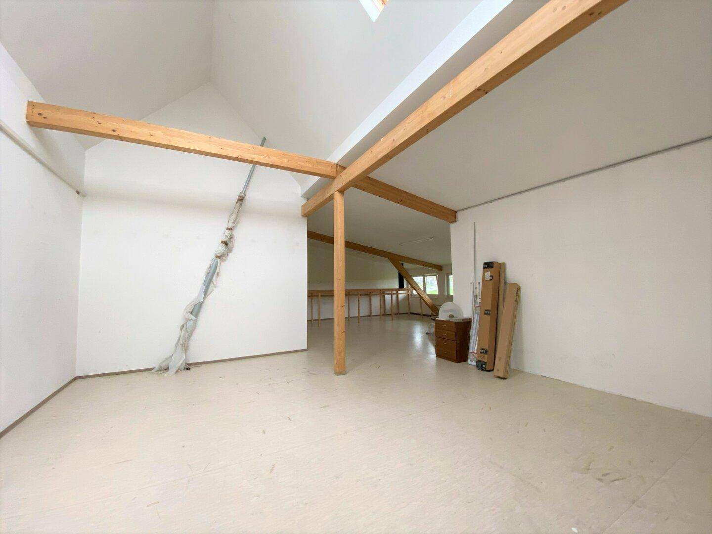 Geräumiger Dachboden mit sichtbaren Holzbalken, hohen Decken und viel natürlichem Licht durch ein Dachfenster.
