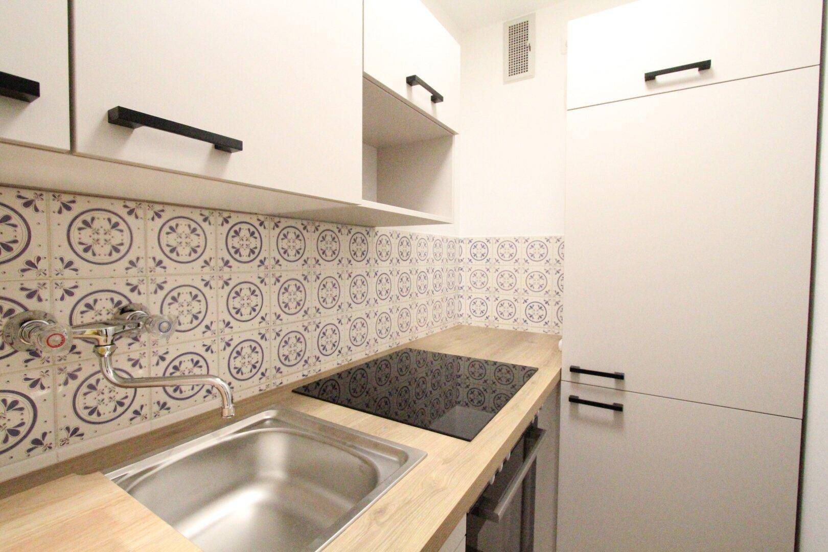 Moderne Küchenzeile mit Induktionskochfeld, Spüle und weißen Schränken, ideal für kleine Wohnungen.
