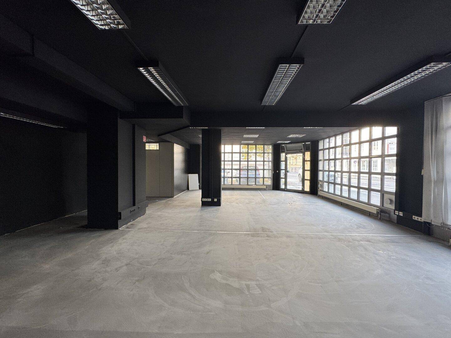 Leerer Verkaufsraum mit schwarzen Wänden und Decke, großen Fenstern und Betonboden, bereit zur Einrichtung.