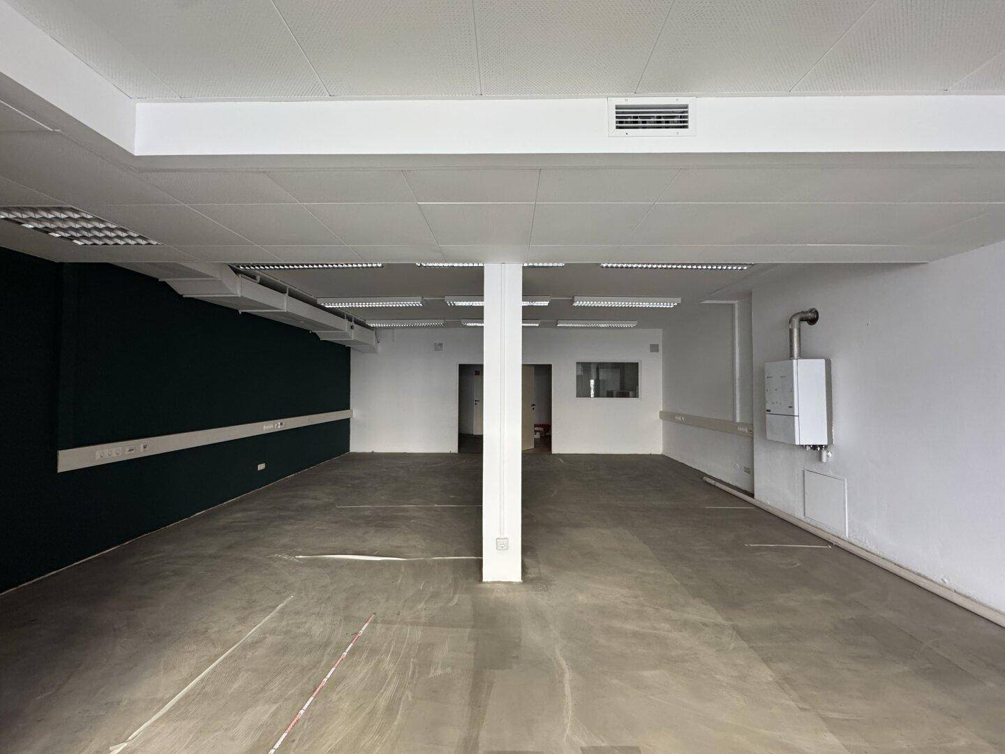 Leerer Gewerberaum mit weißer Decke, Betonboden und einer dunkelgrünen Akzentwand, bereit zur Nutzung.