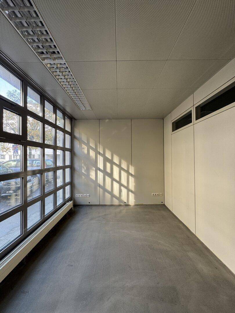 Heller Büroraum mit großen Fenstern, die viel Tageslicht hereinlassen, und einem modernen Betonboden.