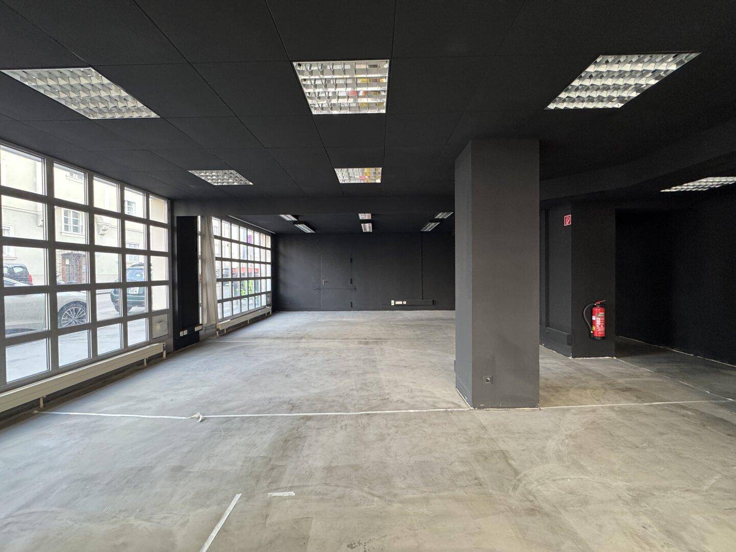 Leerer Verkaufsraum mit schwarzen Wänden und Decke, großen Fenstern und einem robusten Betonboden.