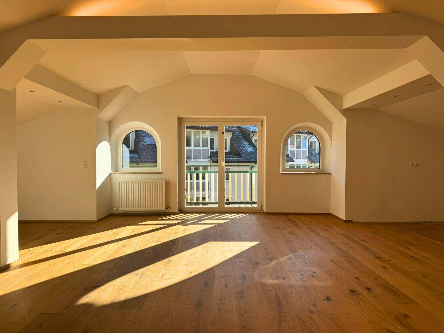 Lichtdurchfluteter Wohnbereich mit Holzboden, hohen Decken und Zugang zum Balkon.