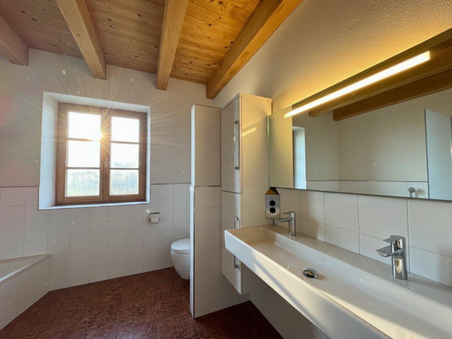 Helles Badezimmer mit Holzbalkendecke, großem Waschbecken und Fenster.