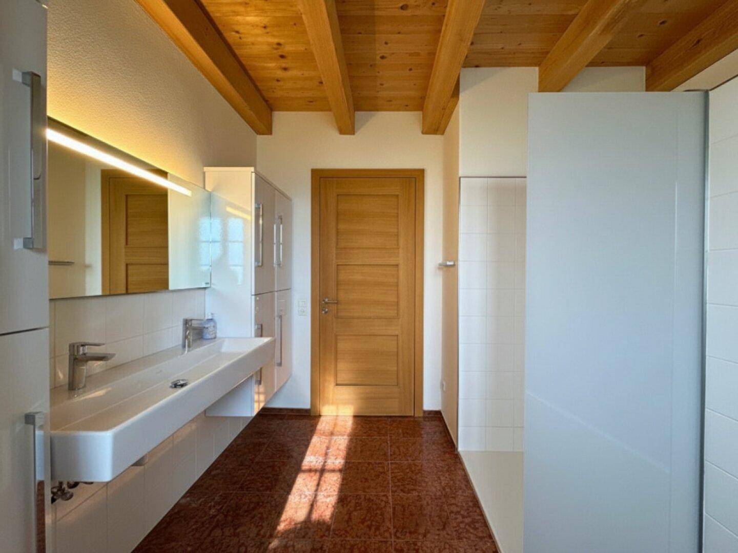 Geräumiges Badezimmer mit Holzbalkendecke, modernem Doppelwaschbecken und Duschbereich.