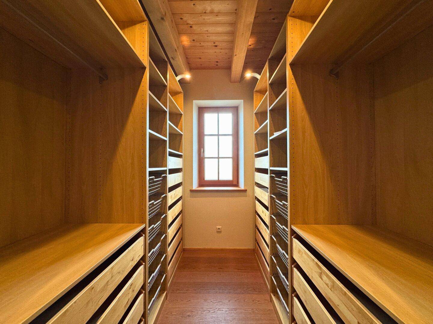 Geräumiger begehbarer Kleiderschrank mit maßgefertigten Holzregalen und Fenster.