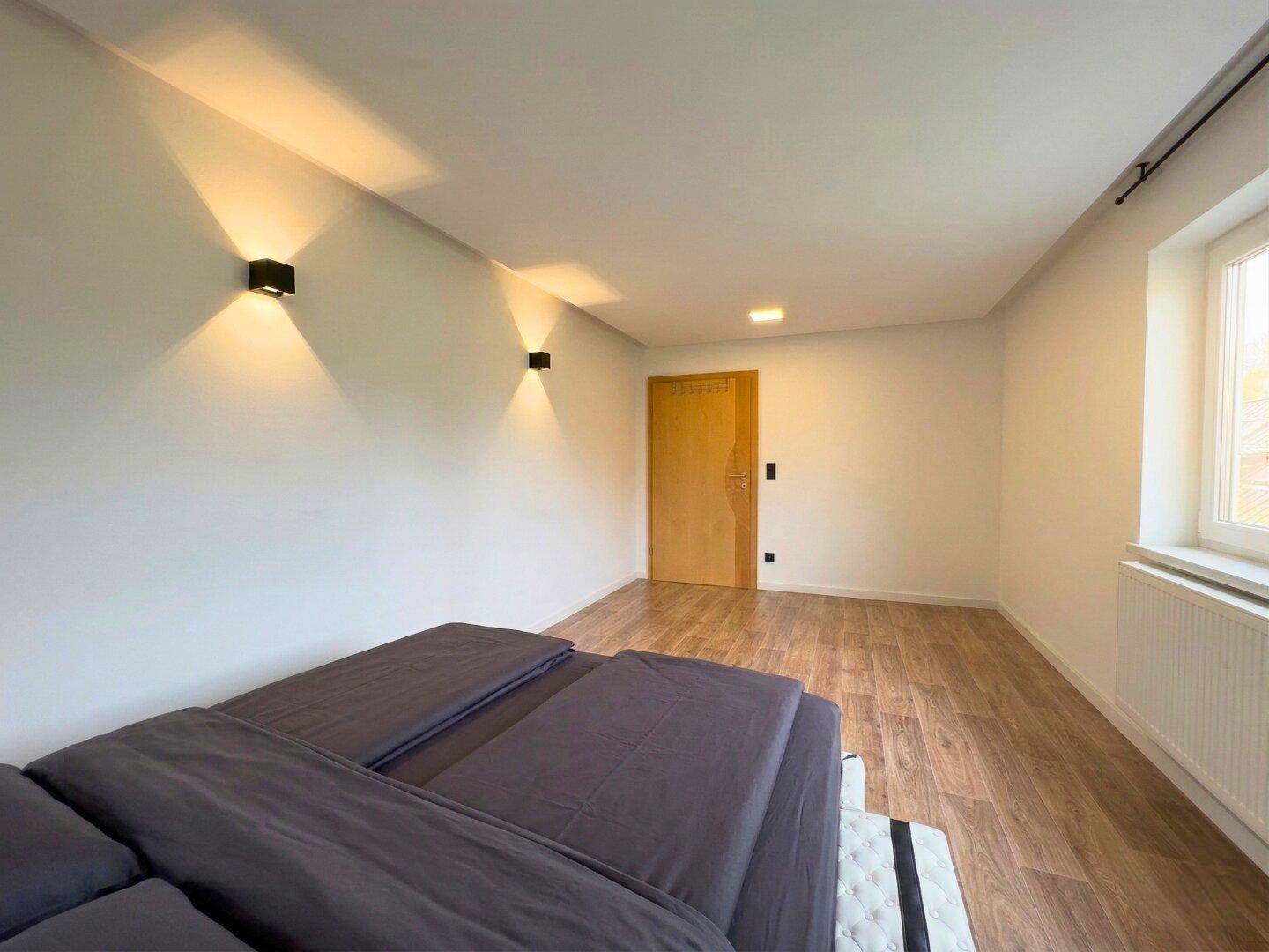 Helles Schlafzimmer mit Holzboden, weiß gestrichenen Wänden und einem Fenster für natürliches Licht.