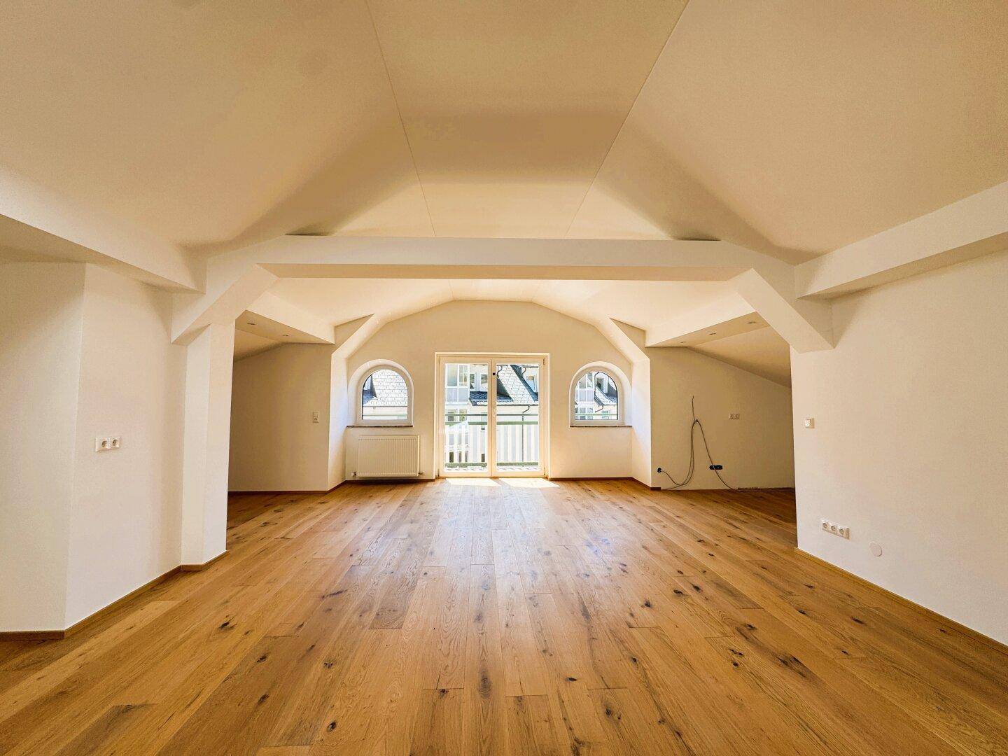 Heller Dachgeschossraum mit Holzboden, Dachschrägen und Zugang zu einem Balkon.