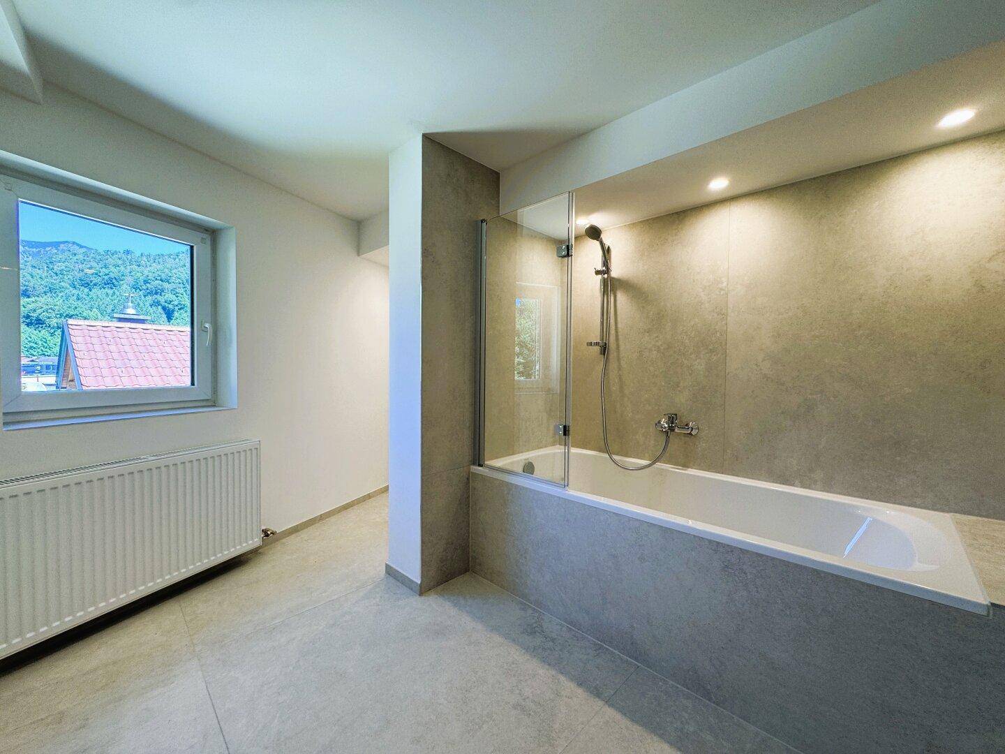 Modernes Badezimmer mit Badewanne, Duschabtrennung und Fenster mit Bergblick.