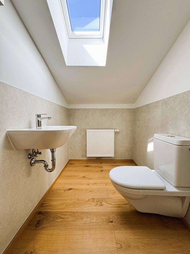 Helles Gäste-WC mit Holzboden, Dachschräge, Waschbecken und Dachfenster.