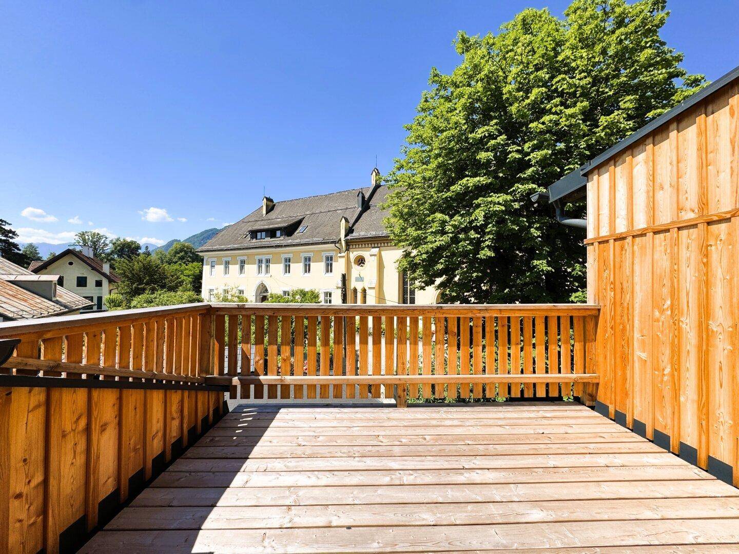 Große Holzterrasse mit Bergblick und Blick auf umliegende Gebäude unter blauem Himmel.