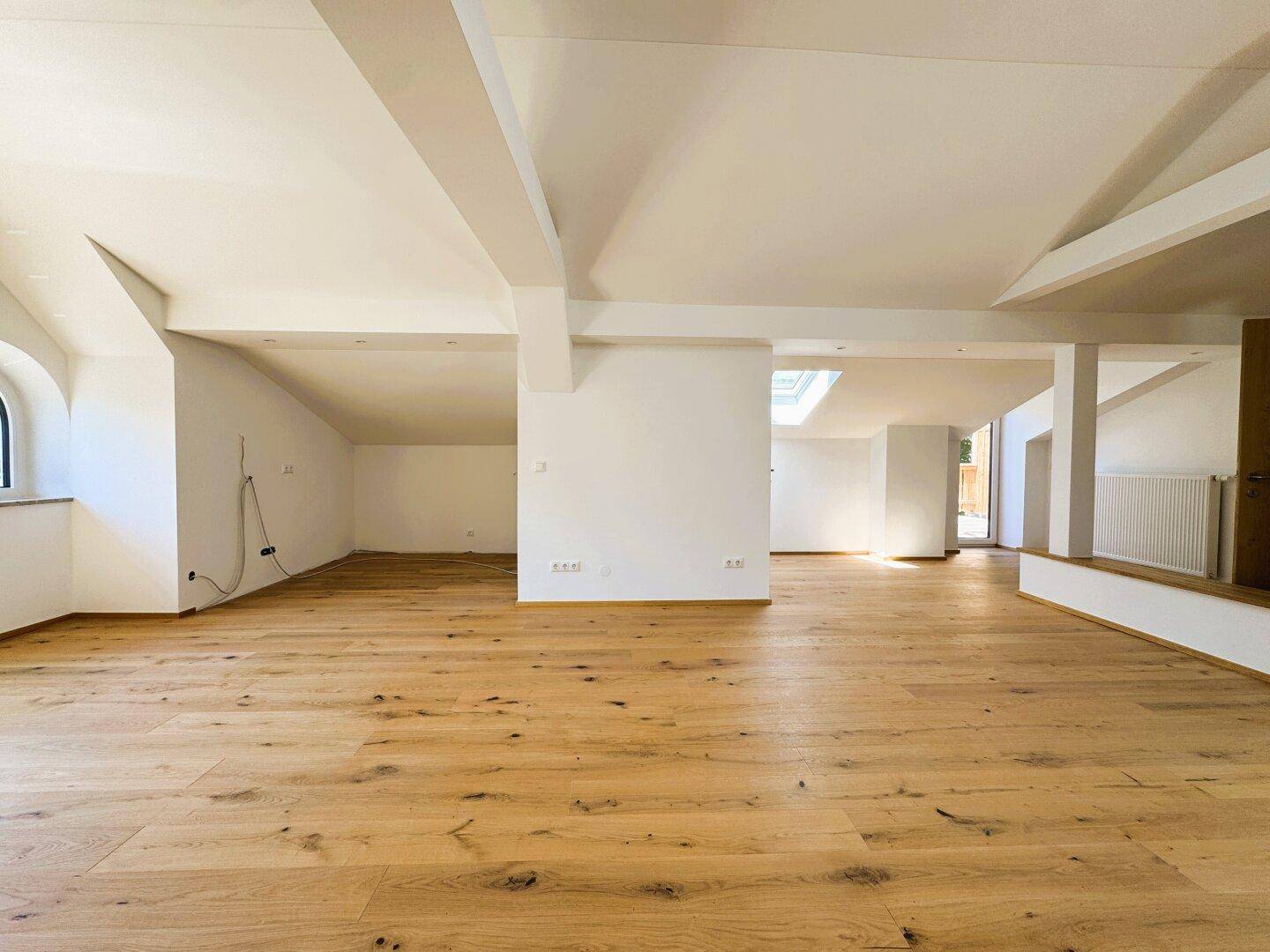 Geräumiger Dachgeschossraum mit Holzboden, Dachschrägen und einem Dachfenster für Tageslicht.