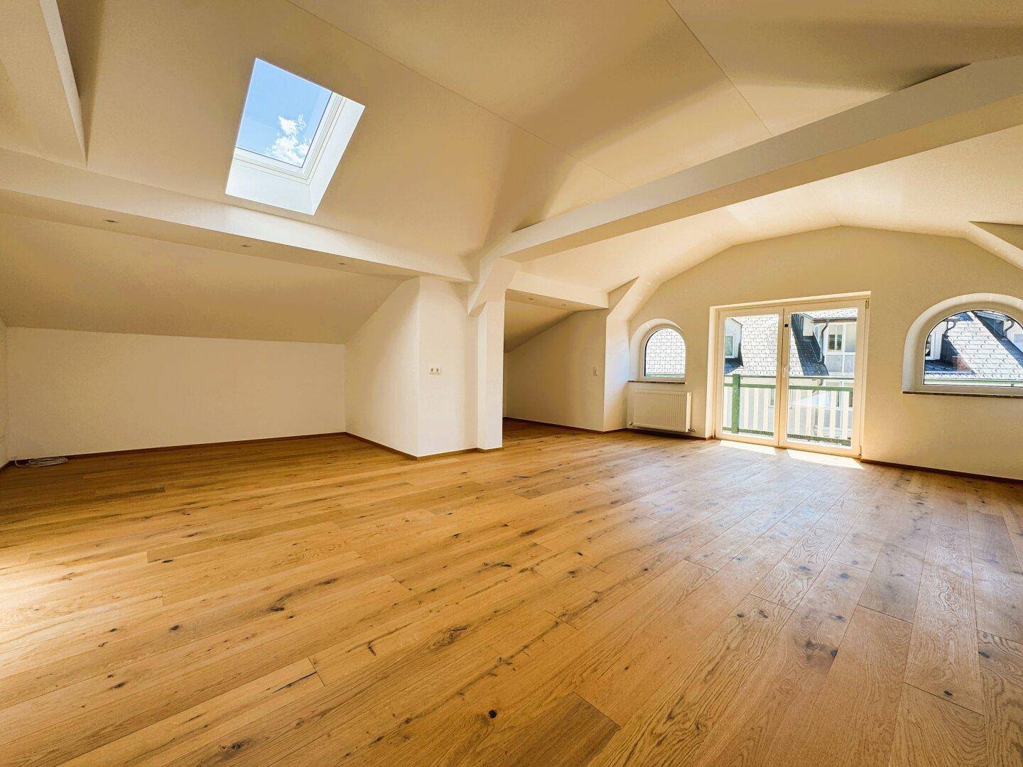 Heller Dachgeschossraum mit Holzboden, Dachfenster und Zugang zu einem Balkon.