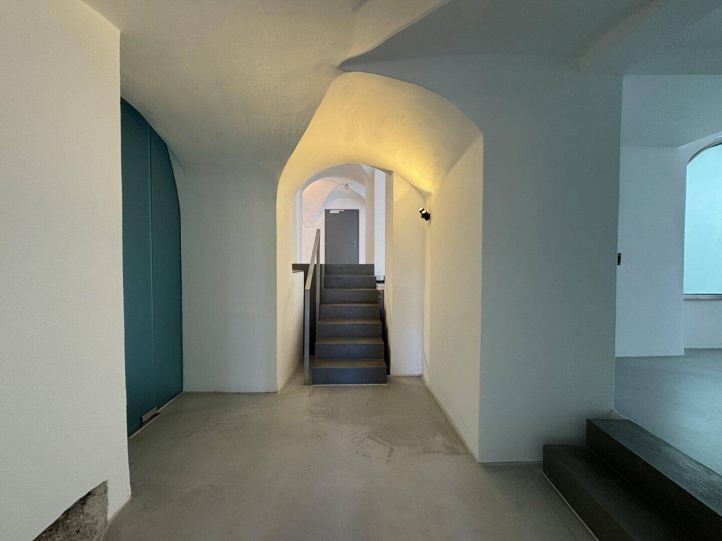 Treppenaufgang in einem Flur mit Gewölbedecken und modernem Bodenbelag, der zu weiteren Räumen führt.