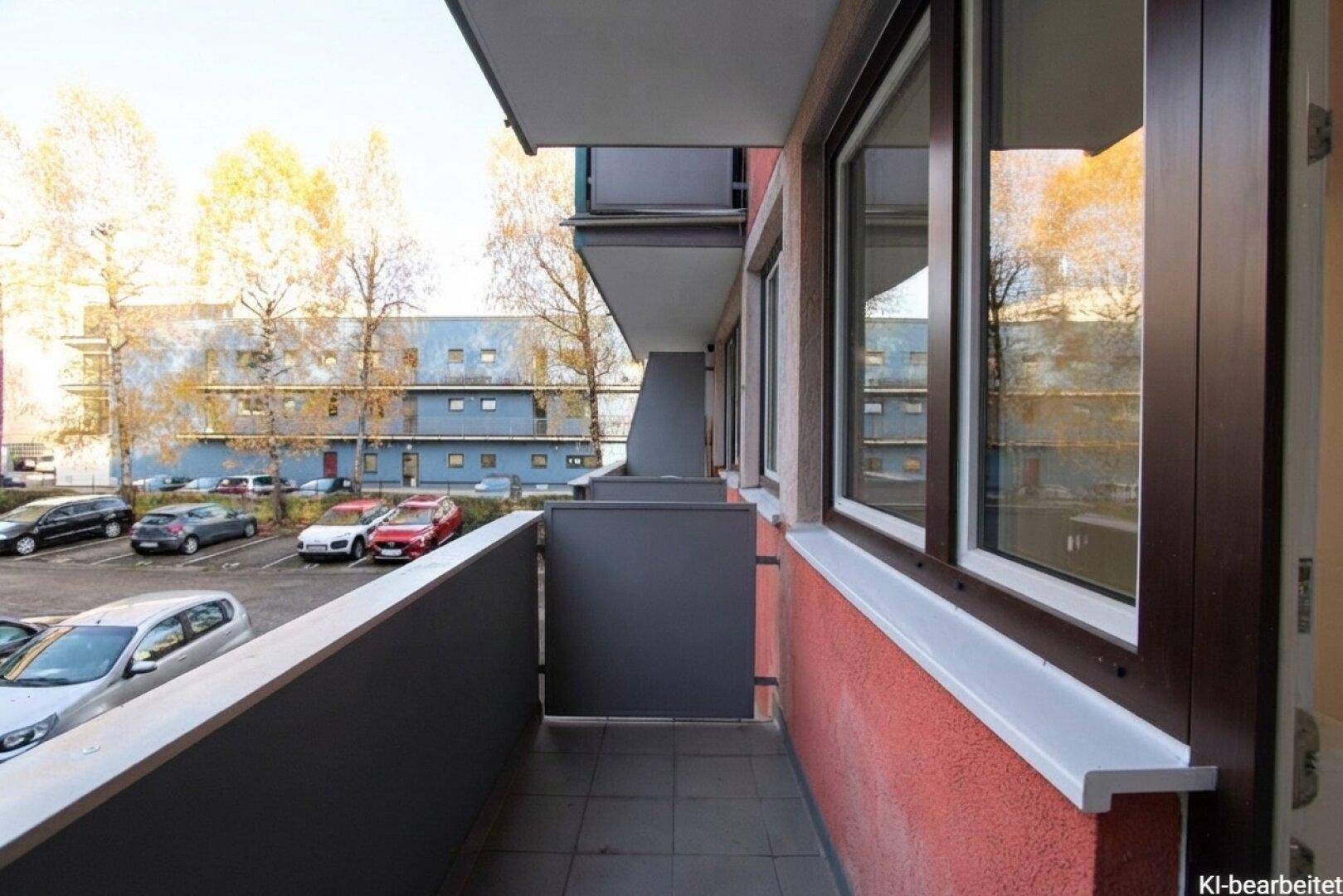 Balkon mit Blick auf den Parkplatz und umliegende Gebäude, mit roter Fassade.